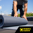 Worker rolling out CrossGrip PVC matting on a rooftop for added slip resistance and membrane protection. Dakota Safety logo visible on mat.