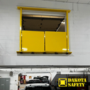 Yellow self-closing mezzanine gate closed across an upper-level roll-up door opening in a service garage.